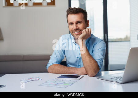 Portrait of handsome web developer looking at camera while sitting in home office Stock Photo