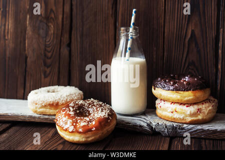 Several donuts and milk in a bottle with a straw on a dark wooden textured rustic background Stock Photo