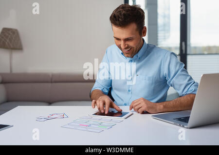 Smiling web developer prototyping in home office with laptop and tablet Stock Photo