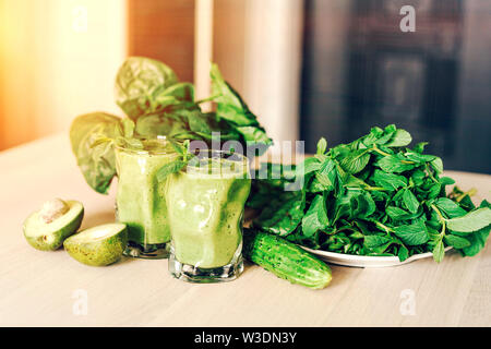 Green ready-made smoothies in glasses, avocado halves and mint leaves, tops of beetroot and spinach on the table Stock Photo
