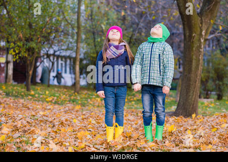 Two smilling children play with maple leaves in park. Boy and girl look up. Stock Photo