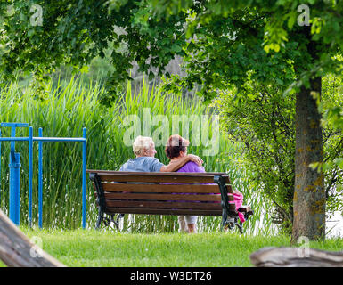 Nyiregyhaza, Hungary. April 19, 2019. Happy senior couple sitting on bench in park. Man and woman resting by the lake Stock Photo