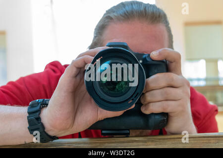 Young man is taking a selfie photo through the mirror with focus on camera lens Stock Photo