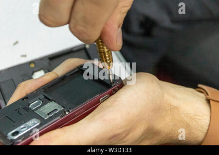 Elderly and young men repair a mobile phone together. They work in a repair shop. They use different tools. They are repair specialists. Stock Photo