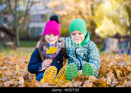 Boy and girl sit during walk in autumn rainy park Stock Photo