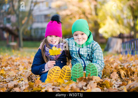 Boy and girl sit during walk in autumn rainy park Stock Photo