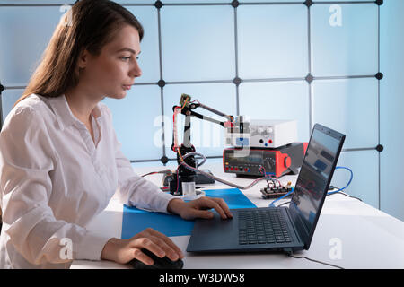 A young woman writes an algorithm for the robot arm. Science Research Laboratory for Robotic Arm Model. Computer Laboratory Stock Photo