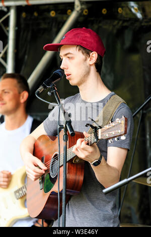 Jake Argyle, young male singer from the Ramsgate band, Argyle, performing on acoustic guitar in front of microphone outdoors at local event. Stock Photo