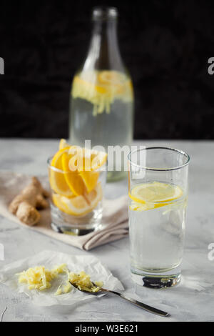 Homemade refreshing infused detox water or lemonade in glass bottles with grated ginger and lemon on dark background close-up.Healthy vegan drink Stock Photo