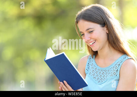 Happy woman reading a blank paper book on green background in a park Stock Photo