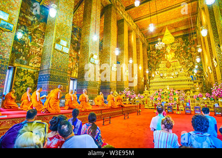 BANGKOK, THAILAND - APRIL 22, 2019: The ubosot with golden Buddha in Wat Pho complex during the pray, monk sit at the special pedestal on the right si Stock Photo