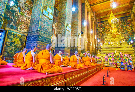 BANGKOK, THAILAND - APRIL 22, 2019: The monks sit on the knees before the ubosot with golden sculpture of Lord Buddha on the top in Wat Pho temple com Stock Photo