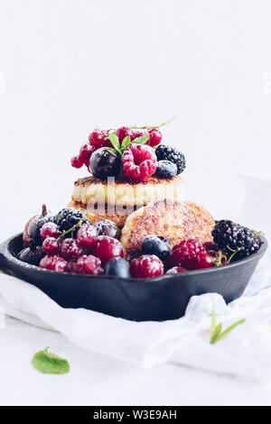 Cottage cheese pancakes served with lots of fresh berries on white background. Gourmet Breakfast - Cottage cheese syrniki, curd fritters with raspberr Stock Photo
