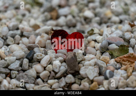 a lonesome red foil heart left on a pebble path after a weddingfocused Stock Photo