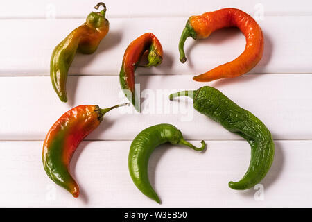 Flat lay Some ugly curved bent chilli peppers on white wooden background. Stock Photo