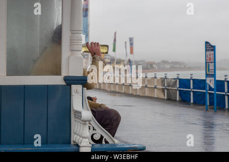 A homeless person drinking a strange coloured liquid on Weymouth seafront Stock Photo