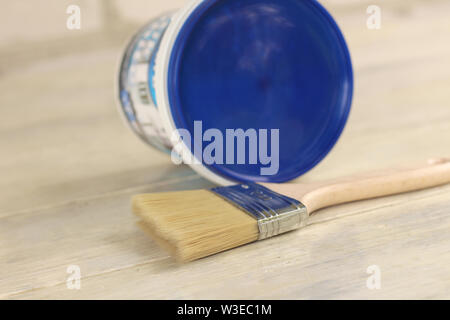 A paint brush is next to a plastic paint bucket with a blue lid on an old white vintage wooden board. Place for text or logo. Stock Photo