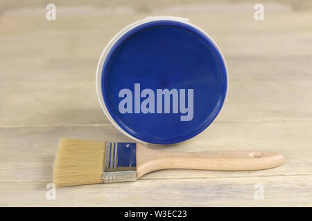 A paint brush is next to a plastic paint bucket with a blue lid on an old white vintage wooden board. Place for text or logo. Stock Photo