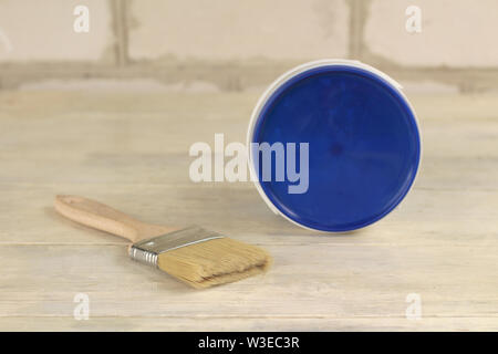 A paint brush is next to a plastic paint bucket with a blue lid on an old white vintage wooden board. Place for text or logo. Stock Photo
