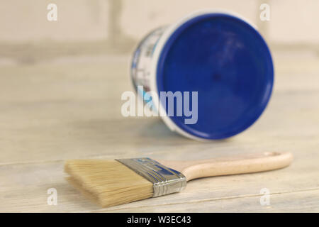 A paint brush is next to a plastic paint bucket with a blue lid on an old white vintage wooden board. Place for text or logo. Stock Photo