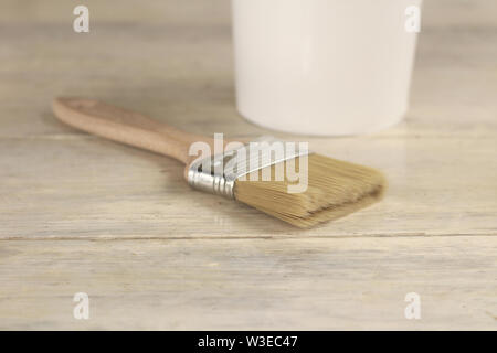 A paint brush is next to a plastic paint bucket with a blue lid on an old white vintage wooden board. Place for text or logo. Stock Photo