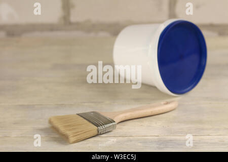 A paint brush is next to a plastic paint bucket with a blue lid on an old white vintage wooden board. Brick wall in the background. Place for text or Stock Photo