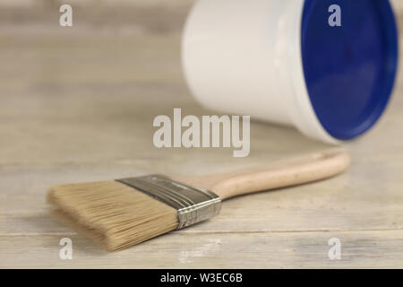 A paint brush is next to a plastic paint bucket with a blue lid on an old white vintage wooden board. Place for text or logo. Stock Photo