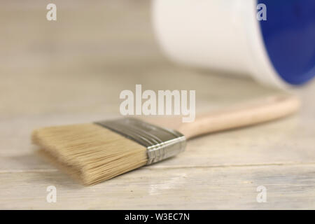 A paint brush is next to a plastic paint bucket with a blue lid on an old white vintage wooden board. Brick wall in the background. Place for text or Stock Photo