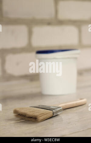A paint brush is next to a plastic paint bucket with a blue lid on an old white vintage wooden board. Brick wall in the background. Place for text or Stock Photo