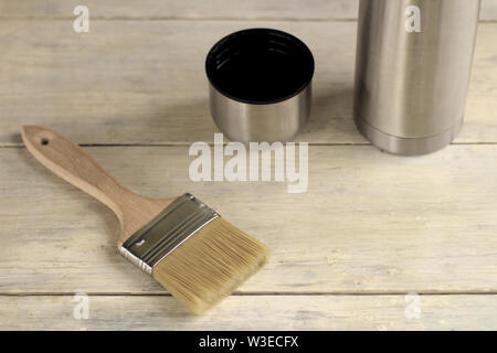 A brush lies next to a thermos with a cup on an old white vintage wooden board. Place for text or logo. Stock Photo