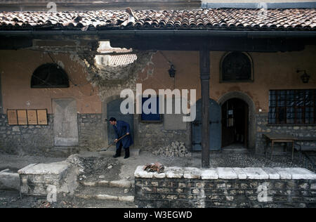 5th April 1993 During the Siege of Sarajevo: in the courtyard of the oldest Orthodox church in Sarajevo, a man shovels up debris below a large hole in the wall made by a mortar bomb or artillery shell. Stock Photo