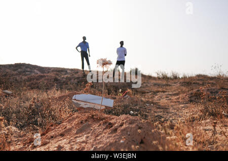 Zarzis, Tunisia. 14th July, 2019. Mamadou Kamarra (l), and Ousmane Koulibali, both from Mali, stand at the 'Cemetery of the Unknown'. Kamarra and Koulibali are two survivors of a recent shipwreck off the Tunisian coast in which 83 people died. On the beaches of the southern Tunisian town of Zarzis, near the holiday island of Djerba, the bodies of drowned migrants are washed up again and again. (to dpa: The Bay of the Nameless Dead) Credit: Simon Kremer/dpa/Alamy Live News Stock Photo