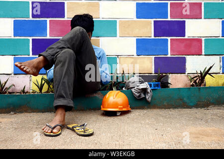 ANTIPOLO CITY, PHILIPPINES – JULY 12, 2019: A construction worker takes off his helmet and rests on a sidewalk. Stock Photo