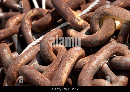 Thick, metal chain with heavy rust deposits and rope at shipyard on dockside Stock Photo