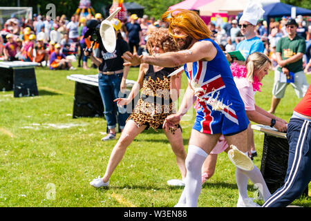 World Custard Pie Championship 2019. The Pie Girls team dressed in fancy dress throwing custard pies from table behind them at unseen opposing team. Stock Photo