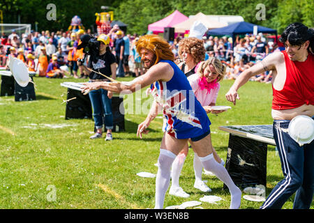 World Custard Pie Championship 2019. The Pie Girls team dressed in fancy dress throwing custard pies from table behind them at unseen opposing team. Stock Photo