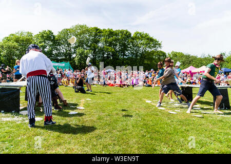 Two teams in fancy dress in field with audience watching, throwing custard pies at each other  during the yearly World Custard Pie Championship 2019. Stock Photo