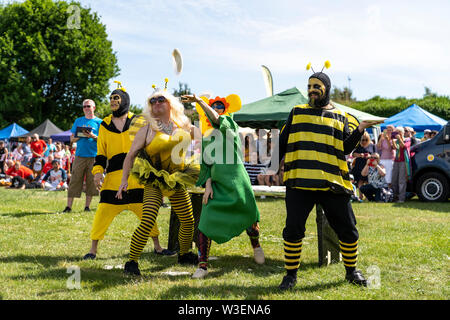 World Custard Pie Championship 2019. The B Team dressed in fancy dress as bees and a flower, throwing custard pies from table behind them. Stock Photo