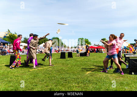 Two teams in fancy dress in field with audience watching, throwing custard pies at each other  during the yearly World Custard Pie Championship 2019. Stock Photo