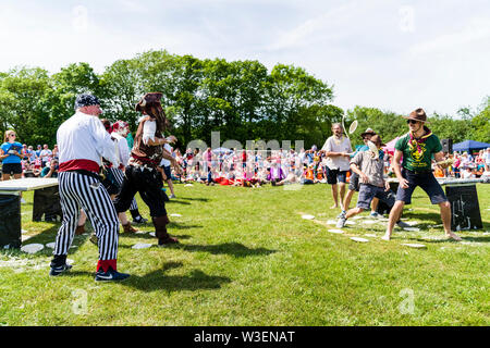 Two teams in fancy dress in field with audience watching, throwing custard pies at each other  during the yearly World Custard Pie Championship 2019. Stock Photo