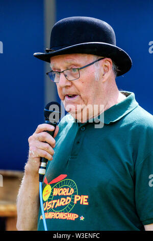 Mike FitzGerald, MBE, holding microphone as he hosts the World Custard Pie Championship. Wears a black bowler hat with green t shirt, close up. Stock Photo