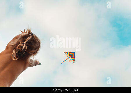 Happy child playing with a kite, child looking up at a multi-colored kite soaring in the sky, happy childhood, enjoying summer holidays Stock Photo