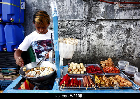 ANTIPOLO CITY, PHILIPPINES – JULY 12, 2019: A street food vendor deep fries fish balls at his food cart and sells them to passers by. Stock Photo