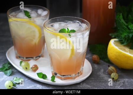 Gooseberry lemonade with mint and ice, a bottle of water and a bottle of gooseberry syrup on a concrete surface. Stock Photo