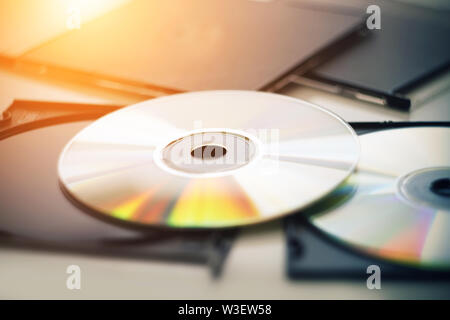 Two new compact disks lie next to the black boxes from the disks, and is illuminated by bright sunlight, from which the disks shimmer in different col Stock Photo
