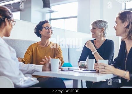 business team sitting at table talking and smiling. Group of business women relaxing during a coffee break in office. Stock Photo