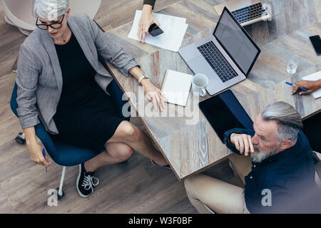 Top view of business people sitting at table looking at presentation. Business team paying attention to the presentation. Stock Photo
