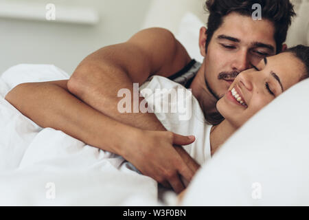 Beautiful happy young couple hugging while sleeping on bed. Young man and woman lying together in bed. Stock Photo