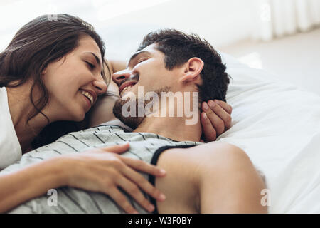 Young couple lying in bed together. Romantic couple in love looking at each other and smiling. Stock Photo
