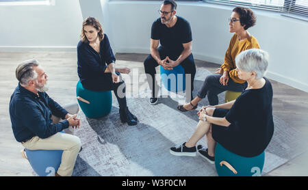 Business team sitting in circle and discussing in the office. Group of people sitting in a lesson on team building. Stock Photo